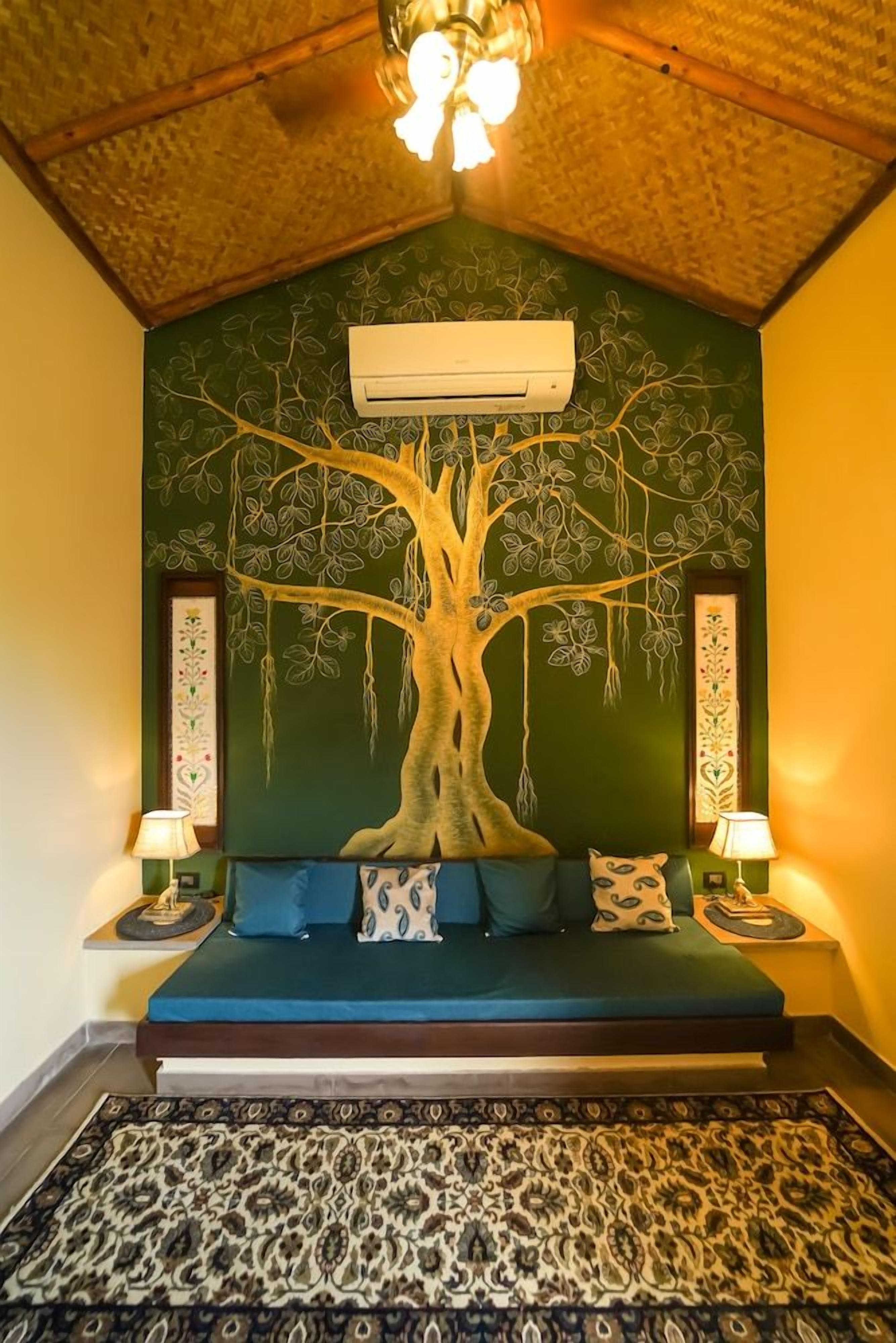 A room with a bed, a wall mural of a tree, an air conditioning unit, and patterned rugs.