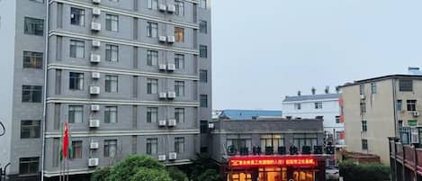 A multi-story building with a ground-level commercial space, parked vehicles, and a flagpole.