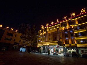 Hotel com vários andares, letreiros iluminados, entrada coberta e estacionamento.