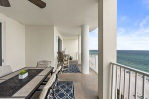 Een balkon met uitzicht op de oceaan, een eettafel met stoelen en een zithoek met een lamp.