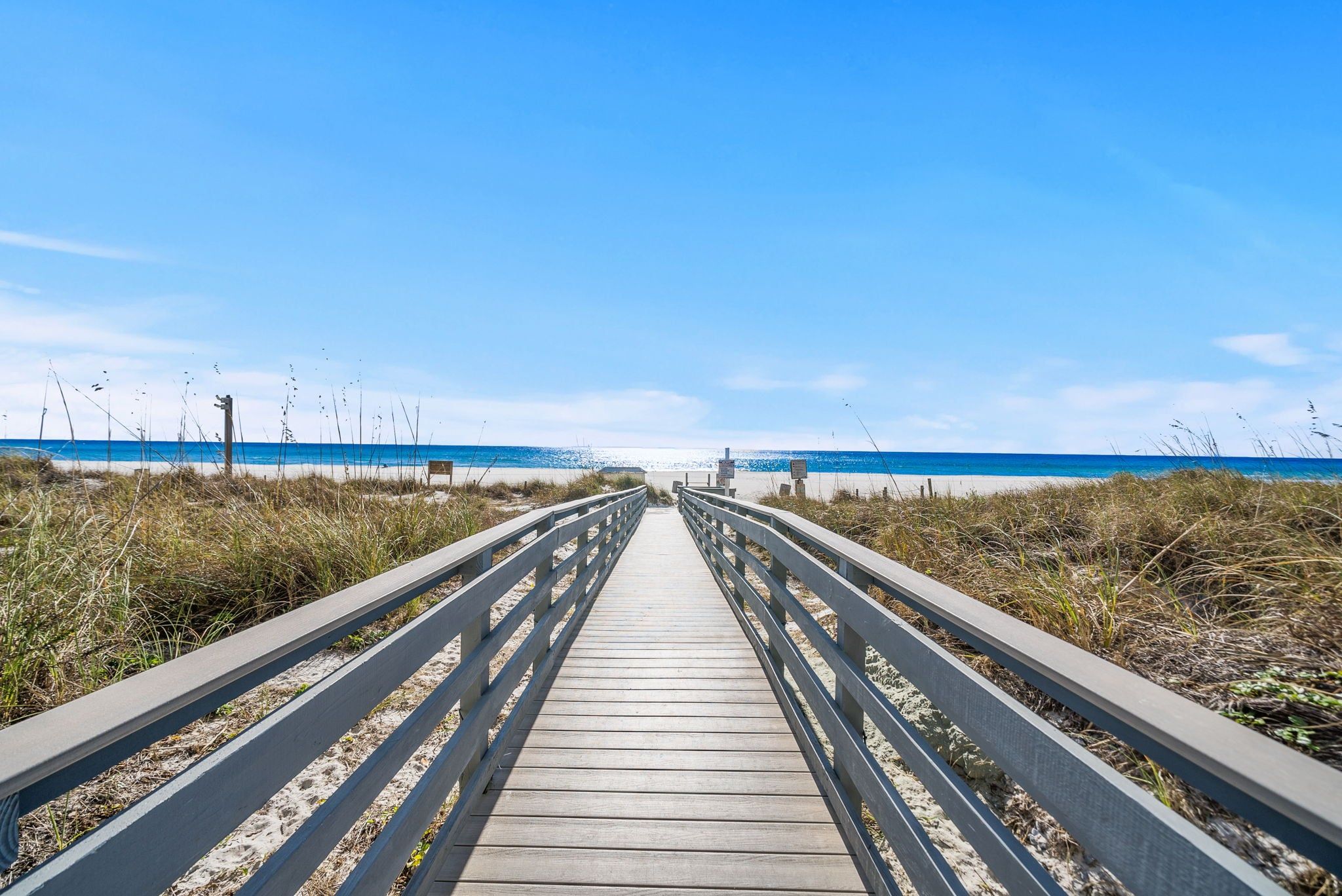 A wooden boardwalk leading to a beach with clear skies.