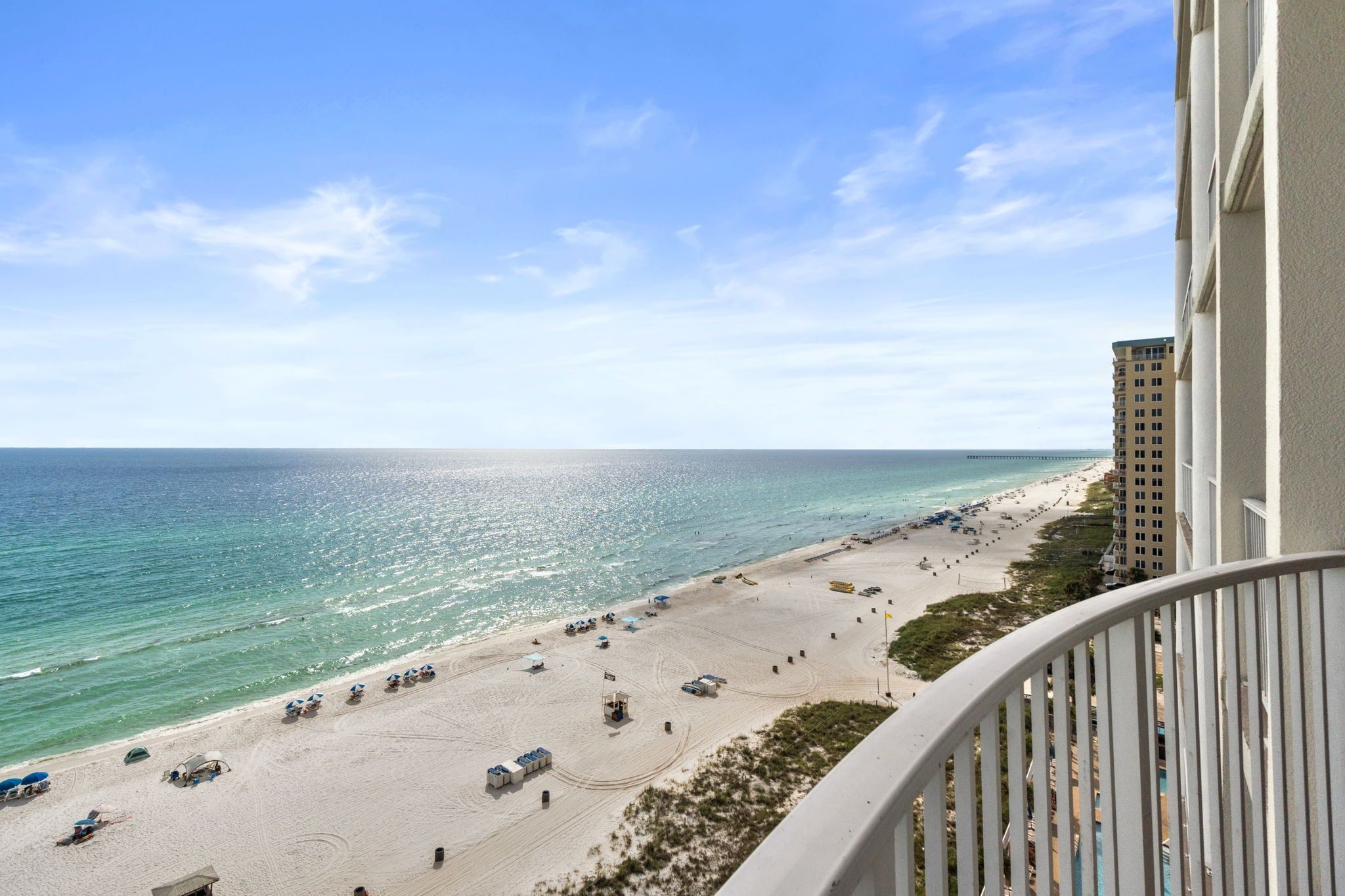 A beach view from a balcony overlooking a sandy beach with a pier in the distance.