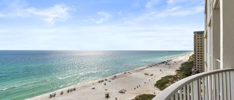 A beach view from a balcony overlooking a sandy beach with a pier in the distance.