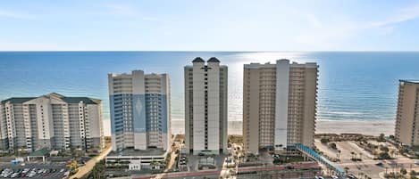 Un complejo hotelero frente a la playa con varios edificios de gran altura, un estacionamiento y un camino que conduce a la playa.