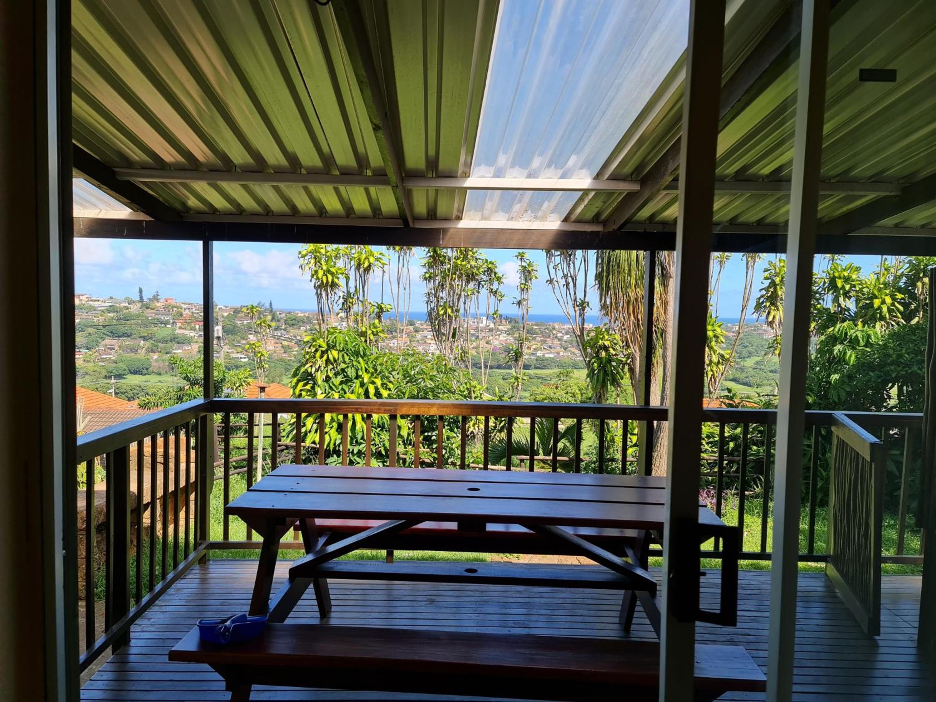 A covered outdoor area with a wooden picnic table and a view of a coastal landscape.