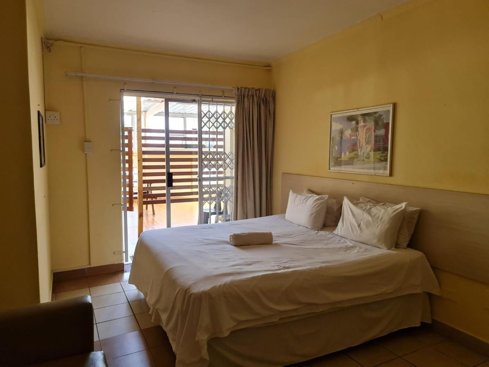 A hotel room with a bed, a painting, and a sliding door leading to an outdoor area.