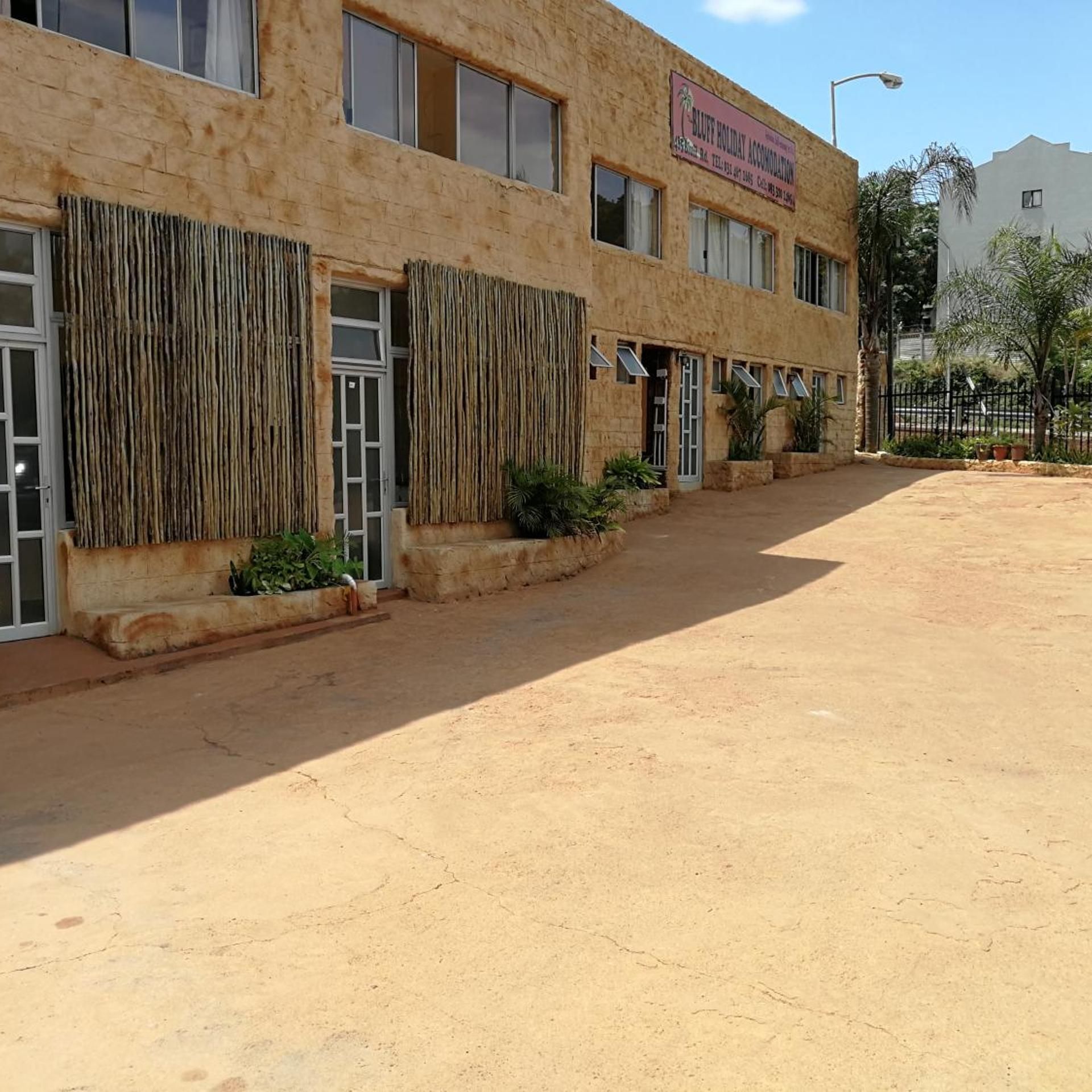 A building with a sign for 'Bluff Holiday Accommodation.' It has multiple windows and doors, with a paved area in front.