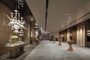 Un moderno vestíbulo de hotel con un mostrador de recepción alargado, luminarias decorativas y una alfombra estampada.