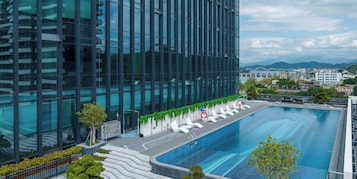 Un edificio moderno con piscina, rodeado de vegetación y vistas a montañas distantes.