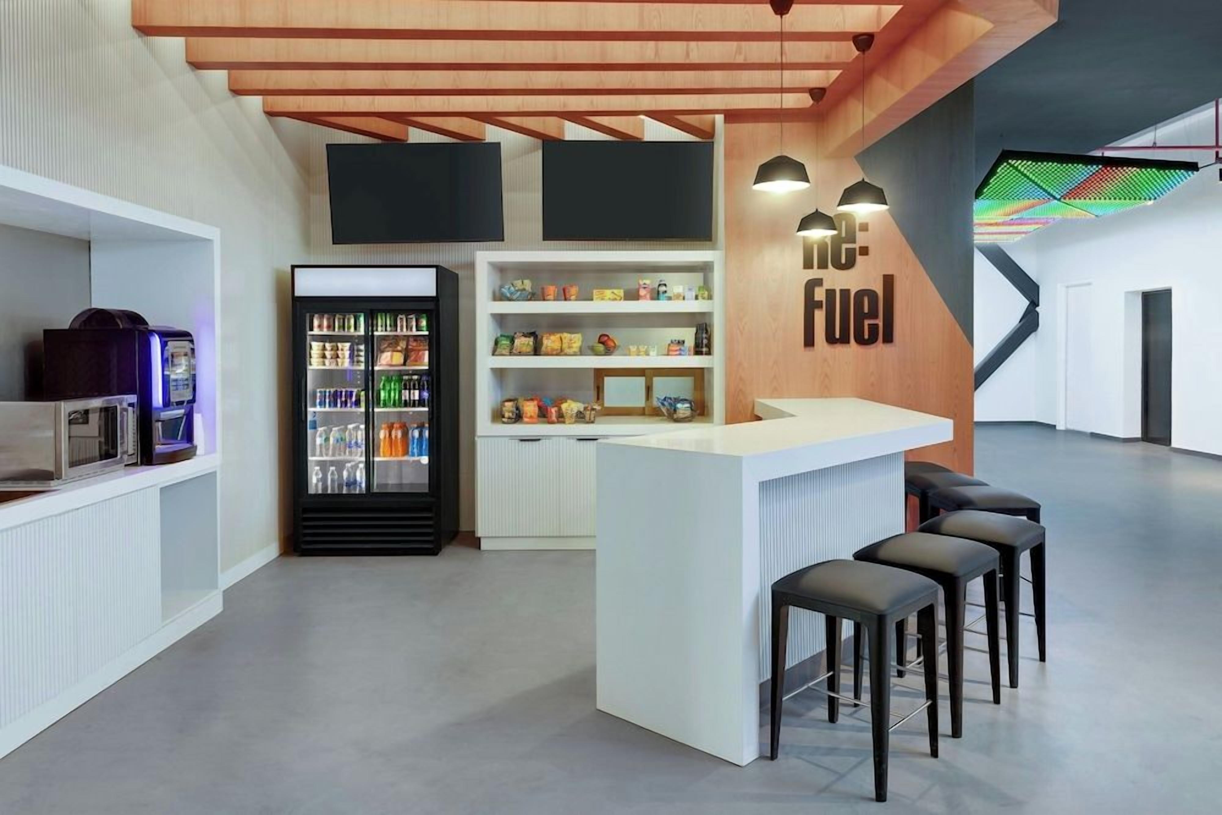 A modern bar area with a counter, stools, and a refrigerator stocked with beverages.