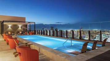 A rooftop pool with lounge chairs and a city view at dusk.