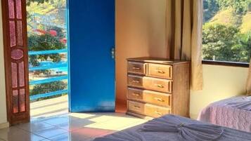 Quarto com cama, penteadeira, televisão e porta que dá para uma varanda.