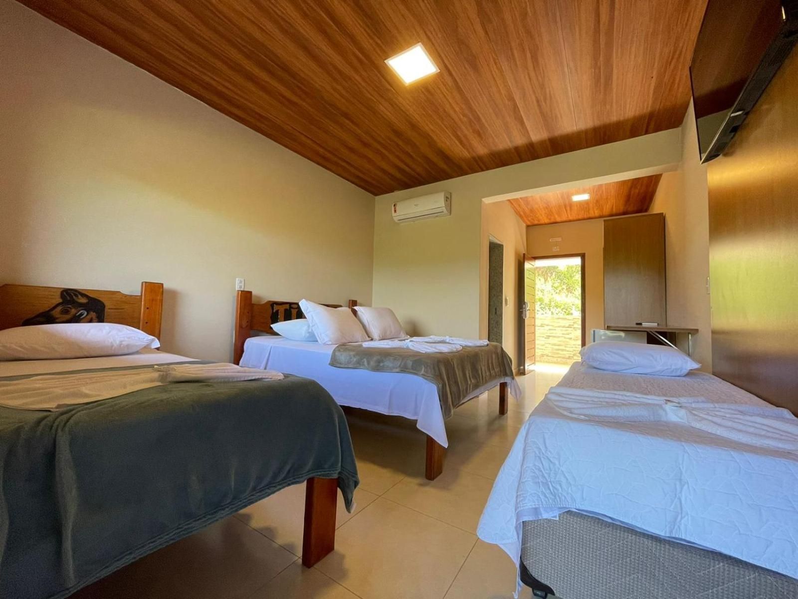 Quarto de hotel com três camas, teto de madeira e vista para o exterior.