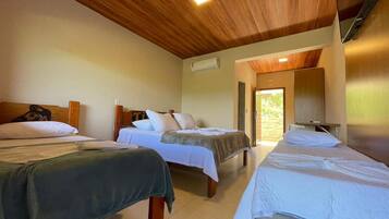 Quarto de hotel com três camas, teto de madeira e vista para o exterior.