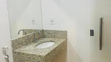 Casa de banho com lavatório de granito, espelho, sanita e cabine de duche.
