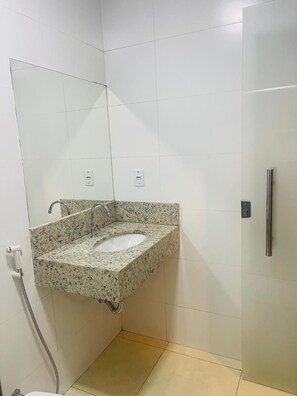 A bathroom with a granite sink, a mirror, a toilet, and a shower stall.