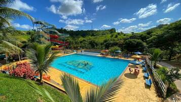 Piscina com escorrega aquático, rodeada por palmeiras e uma paisagem montanhosa.