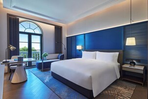 Una habitación de hotel moderna con una cama grande, un escritorio con lámpara, una zona de estar y vistas por la ventana.