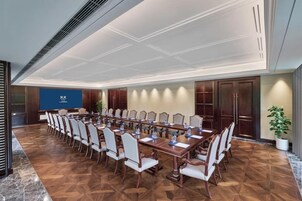 Un salón de conferencias con una larga mesa, sillas y una pantalla.