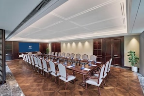 Un salón de conferencias con una larga mesa, sillas y una pantalla.