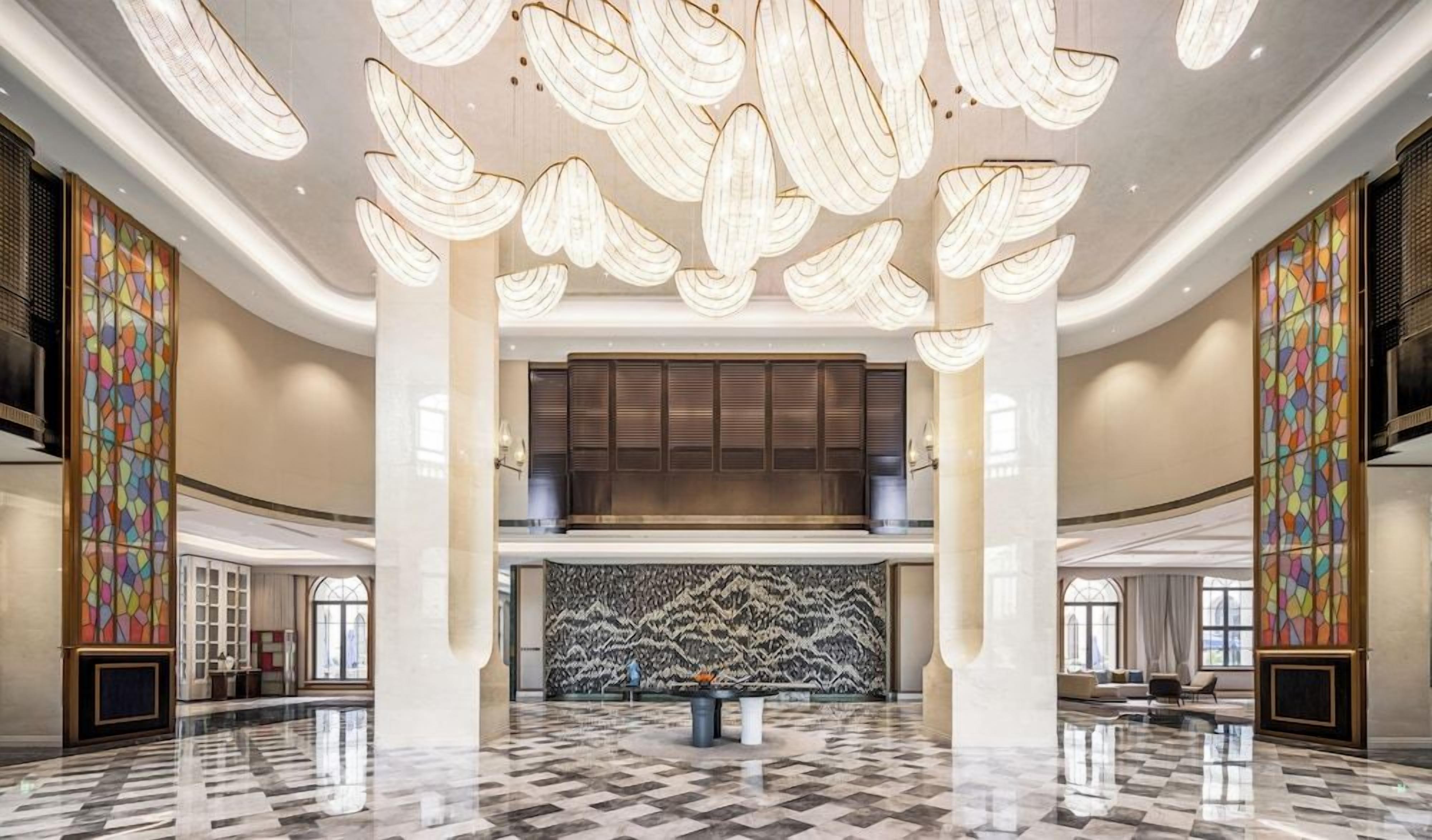 Un vestíbulo amplio con techo alto, grandes candelabros, una zona de estar central y un diseño de pared con motivos.