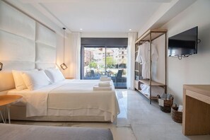 A modern hotel room with a large bed, a TV mounted on the wall, and a view of the city through the window. - Thetis Boutique Luxury Apartments (Sithonia)