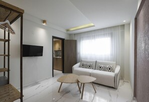 A modern living room with a sofa, two small tables, a TV mounted on the wall, and a wooden staircase. - Thetis Boutique Luxury Apartments (Sithonia)