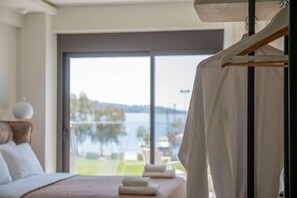 A bedroom with a large window, a bed, a hanging towel, and a view of a body of water. - Thetis Boutique Luxury Apartments (Sithonia)