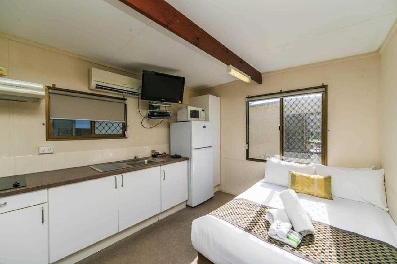 A compact hotel room with a kitchenette, a bed with a checkered bedspread, and a window with a view.