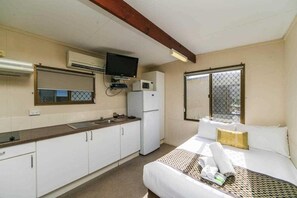 A compact hotel room with a kitchenette, a bed with a checkered bedspread, and a window with a view. - Reflections Holiday Parks Lennox Head (Ballina)