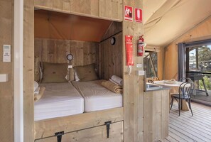 Ein gemütlicher Holzraum mit zwei Betten, einem kleinen Tisch, Stühlen und einem Fenster mit Blick auf eine Terrasse.