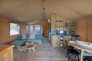 A tented accommodation with a kitchenette, a dining area, and a seating area with a sofa and tables. - Reflections Holiday Parks Lennox Head (Ballina)