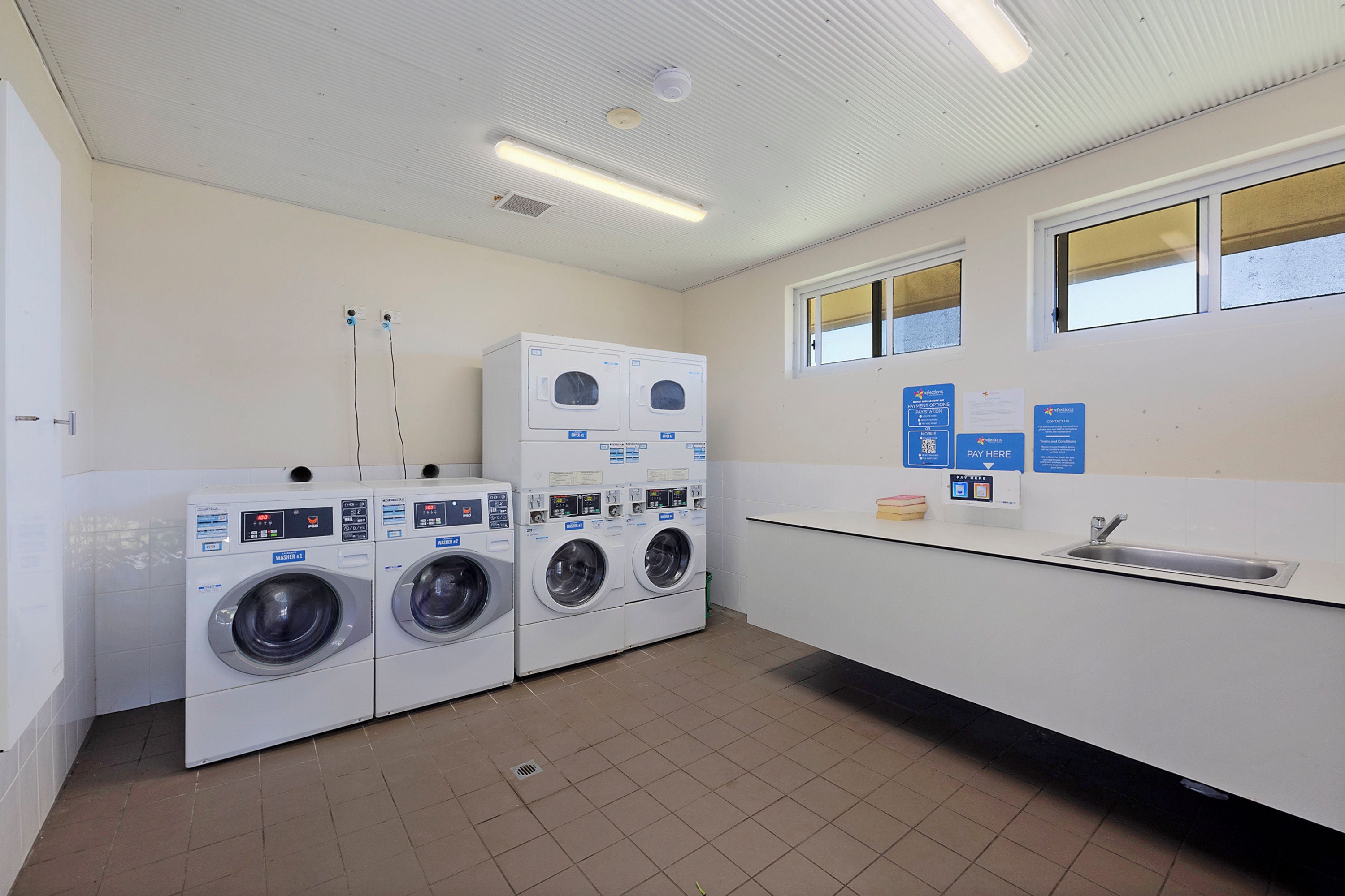 A laundry facility with multiple washing machines, a sink, and payment options.