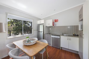 A modern kitchen with white cabinets, a stainless steel refrigerator, a dishwasher, and a window overlooking greenery. - Reflections Holiday Parks Lennox Head (Ballina)