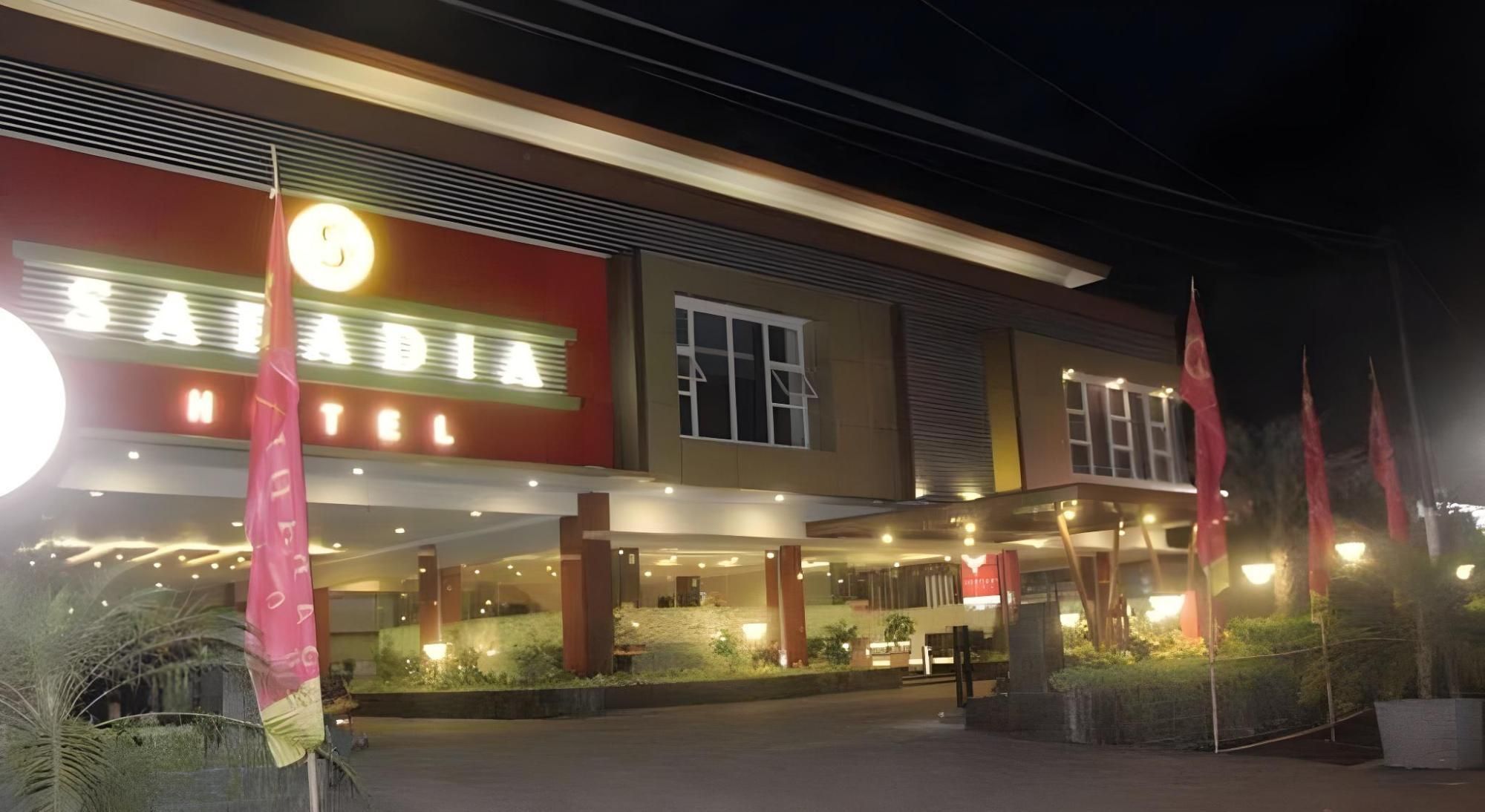 A hotel with a prominent sign, a covered entrance, and a landscaped area with plants.
