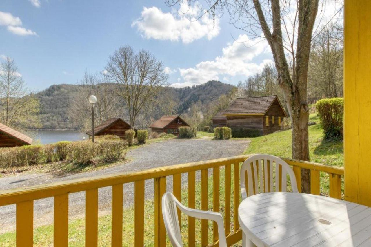 A lakeside property with wooden cabins, a yellow railing, and a table with chairs.