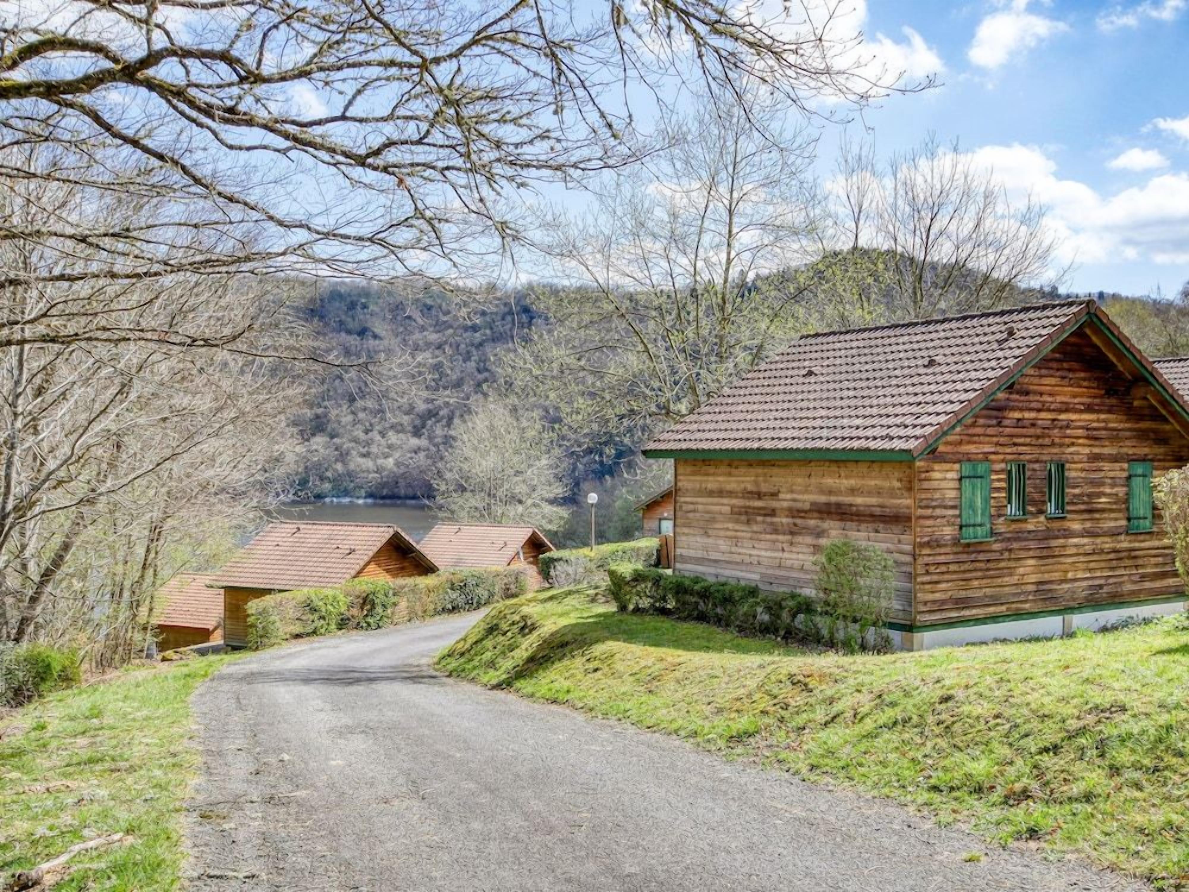 A wooden cabin with a sloped roof, surrounded by a gravel driveway and a grassy area.