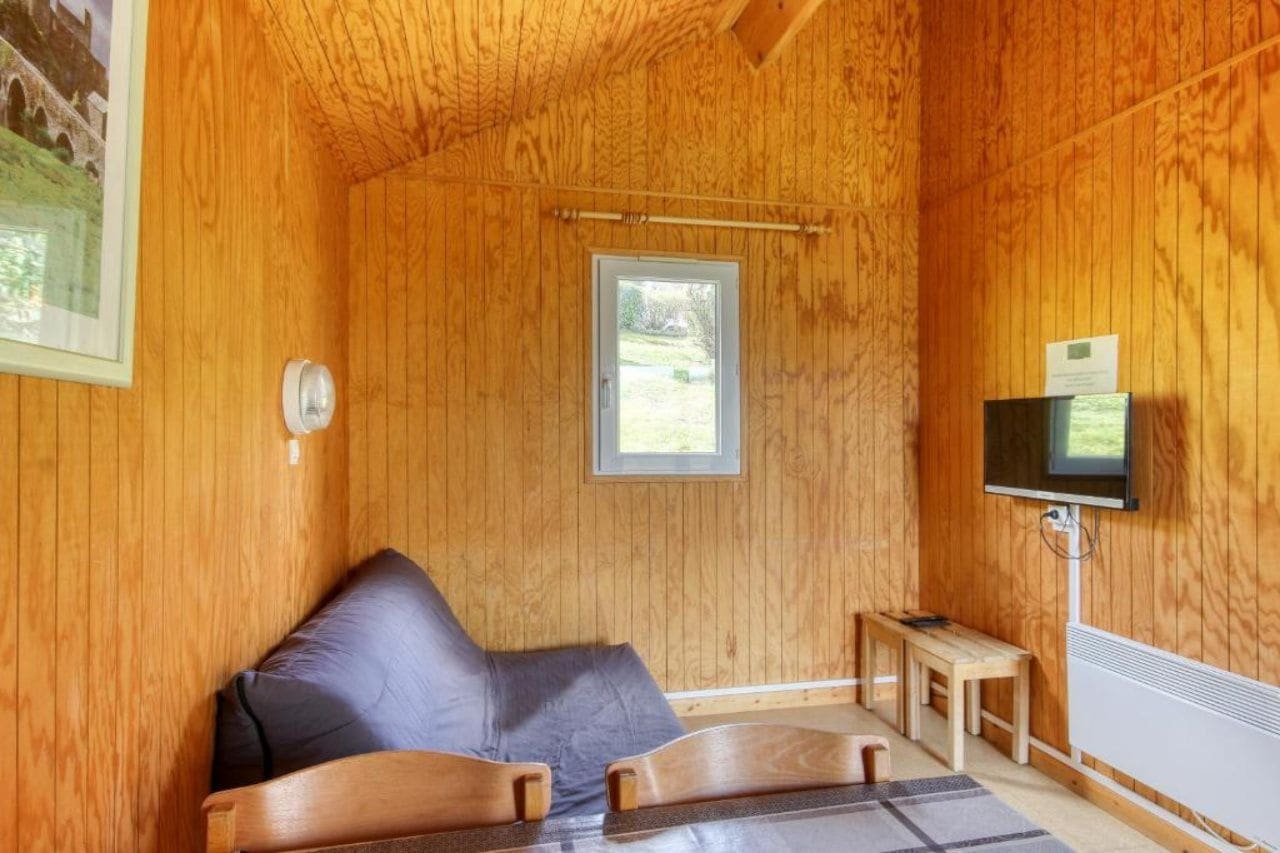 A wooden room with a bed, a television, and a window.
