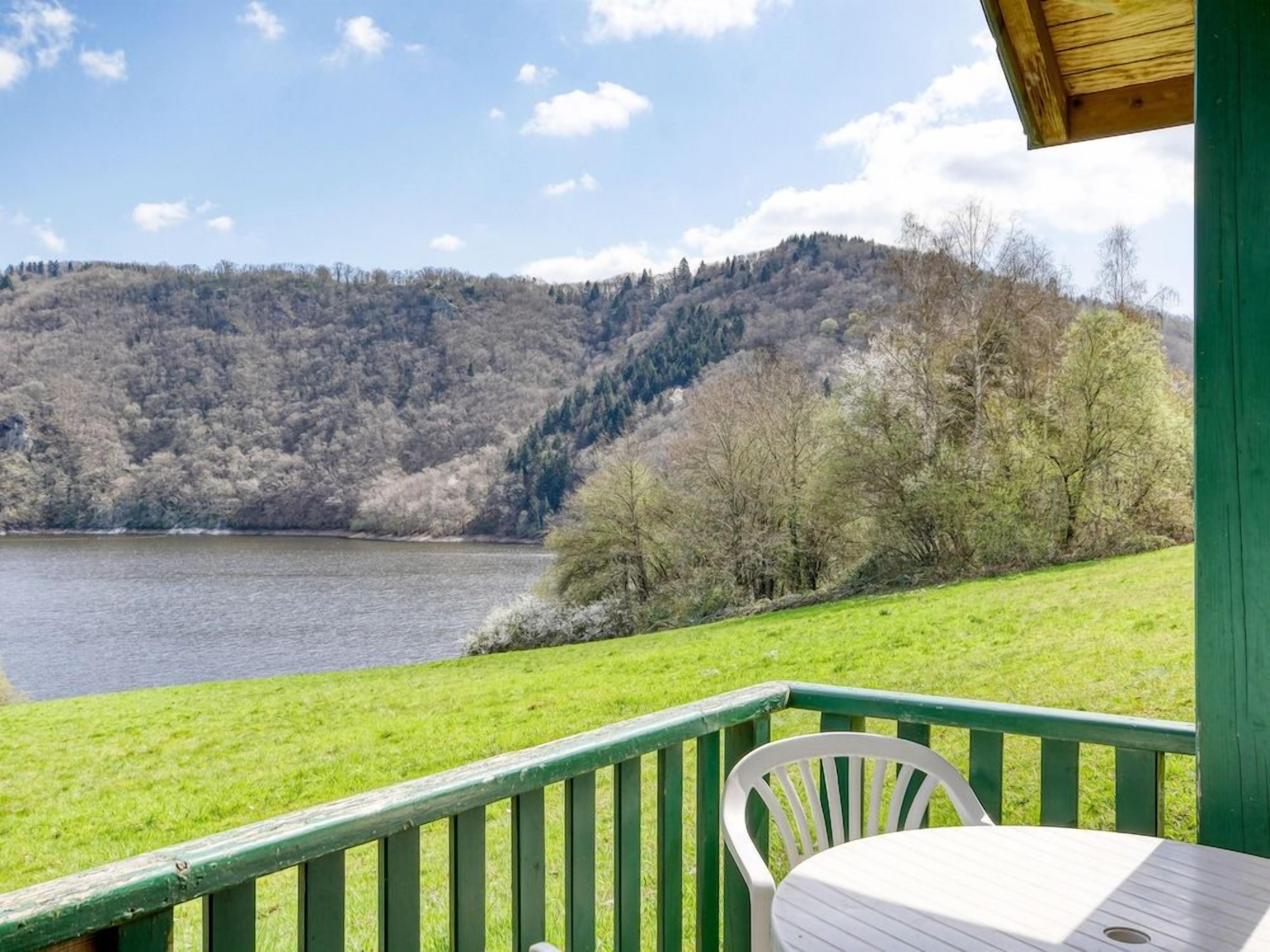 A lakeside view with a wooden deck, a white chair, and a table.