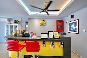 A reception area with a counter, two red bar stools, a ceiling fan, framed certificates, a red cabinet, and a wall-mounted security camera.