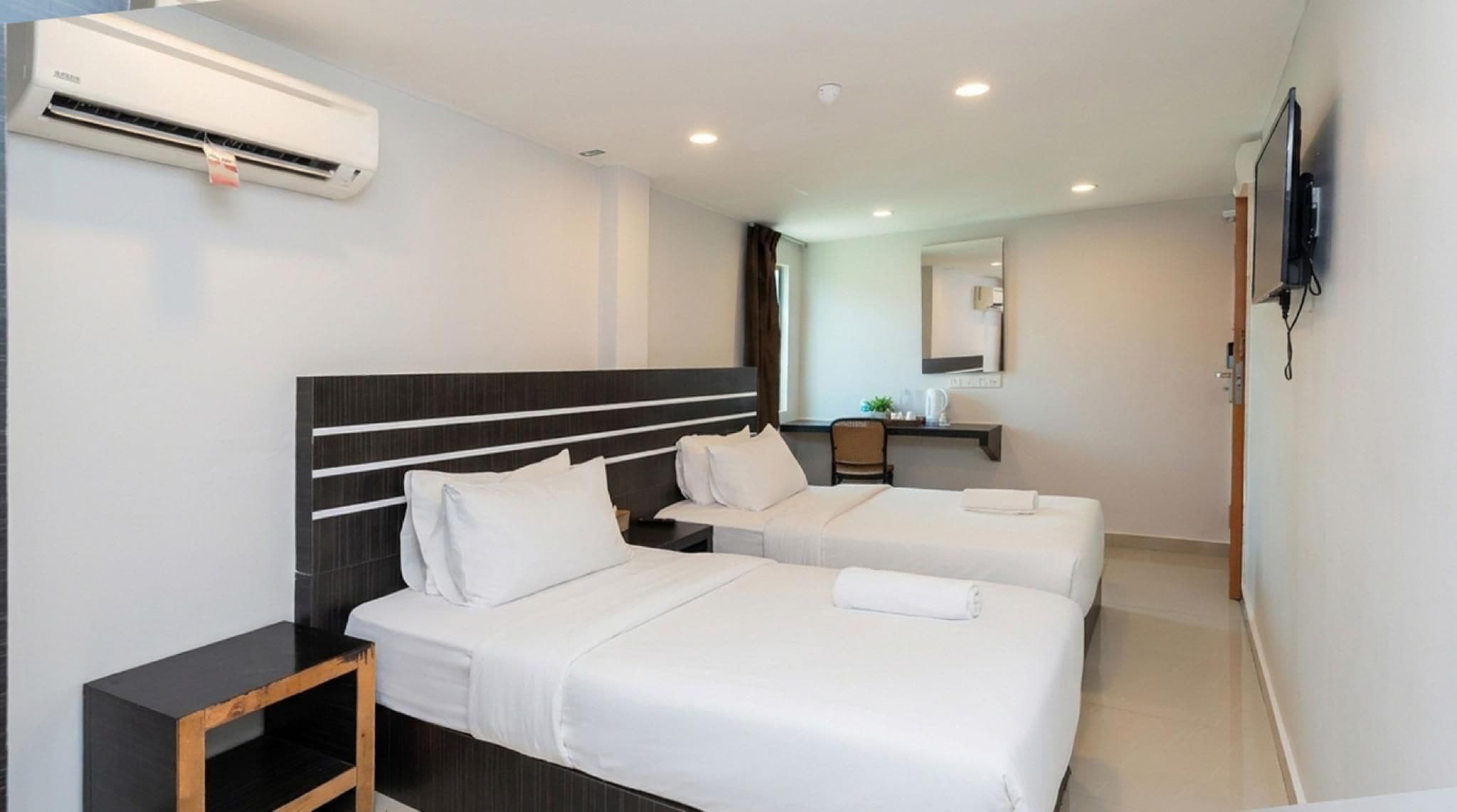 Hotellihuone, jossa on kaksi sänkyä, työpöytä, tuoli, taulutelevisio ja ilmastointilaite.