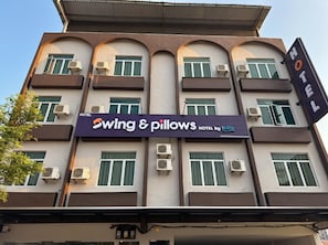 A hotel building with multiple balconies, air conditioning units, and a prominent sign for 'Swing & Pillows Hotel by Iovita.'