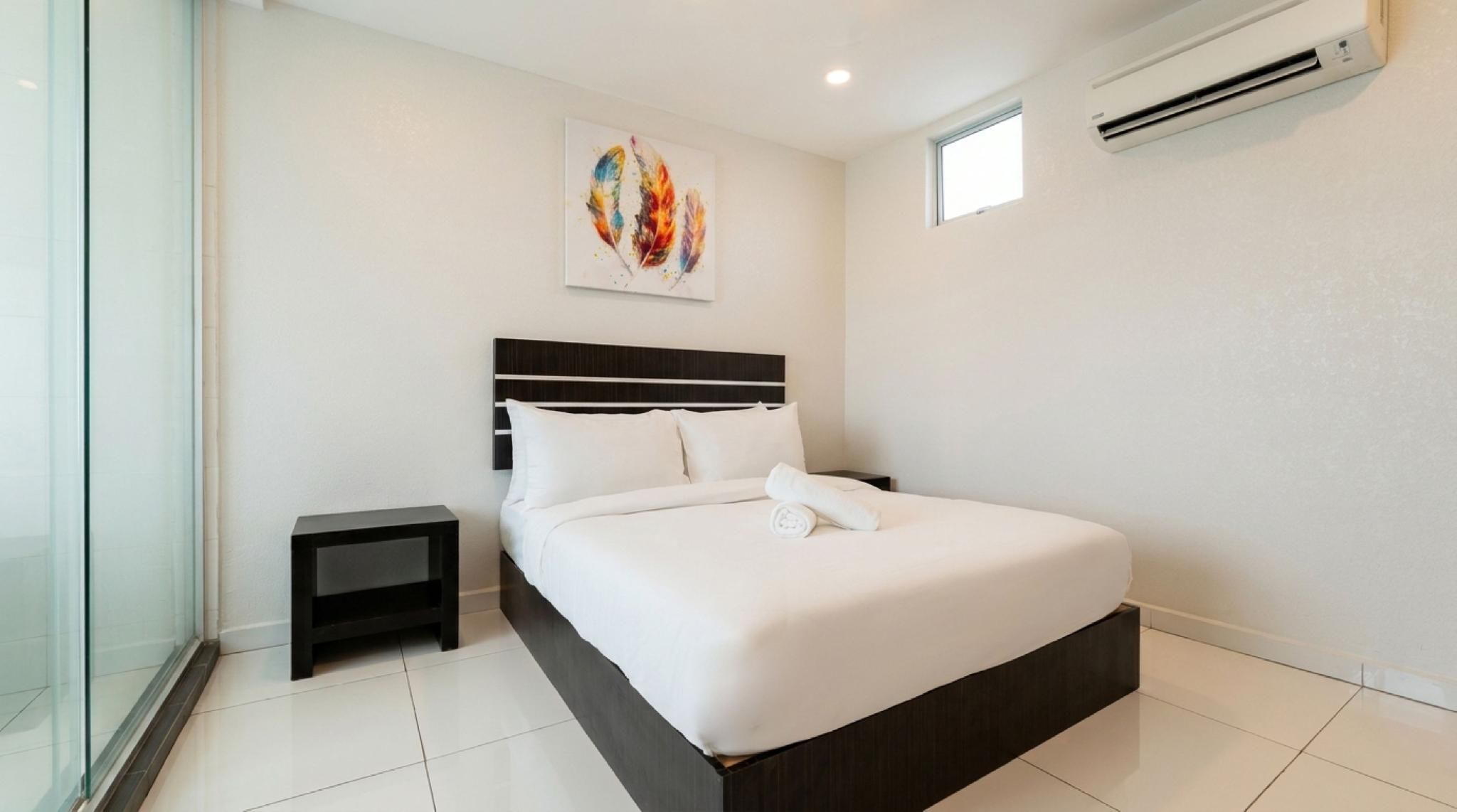 A modern hotel room with a large bed, a small bedside table, a wall-mounted air conditioner, and a window.