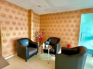 A room with a patterned wall, two black armchairs, a small round table with a vase of flowers, and a red fire extinguisher.
