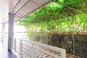 A covered outdoor area with a metal railing, greenery, and a stone wall.