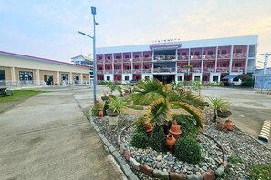 A multi-story hotel with a red facade, a parking area, and landscaped gardens with palm trees and potted plants. - EC Hotel Near Laoag Airport by Zuzu (Laoag)