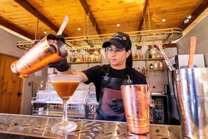 Un barman prépare un cocktail derrière un comptoir, avec différentes bouteilles et différents verres à portée de main.