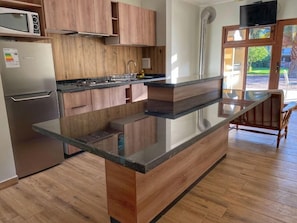 Una cocina moderna con armarios de madera, un refrigerador de acero inoxidable, un microondas y una encimera-isla de vidrio.
