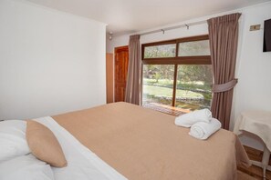 Una habitación de hotel con cama, ventana con cortinas y vista a un jardín, además de una pequeña mesa con silla.