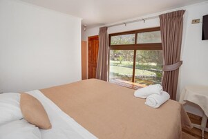 Una habitación de hotel con cama, ventana con cortinas y vista a un jardín, además de una pequeña mesa con silla.